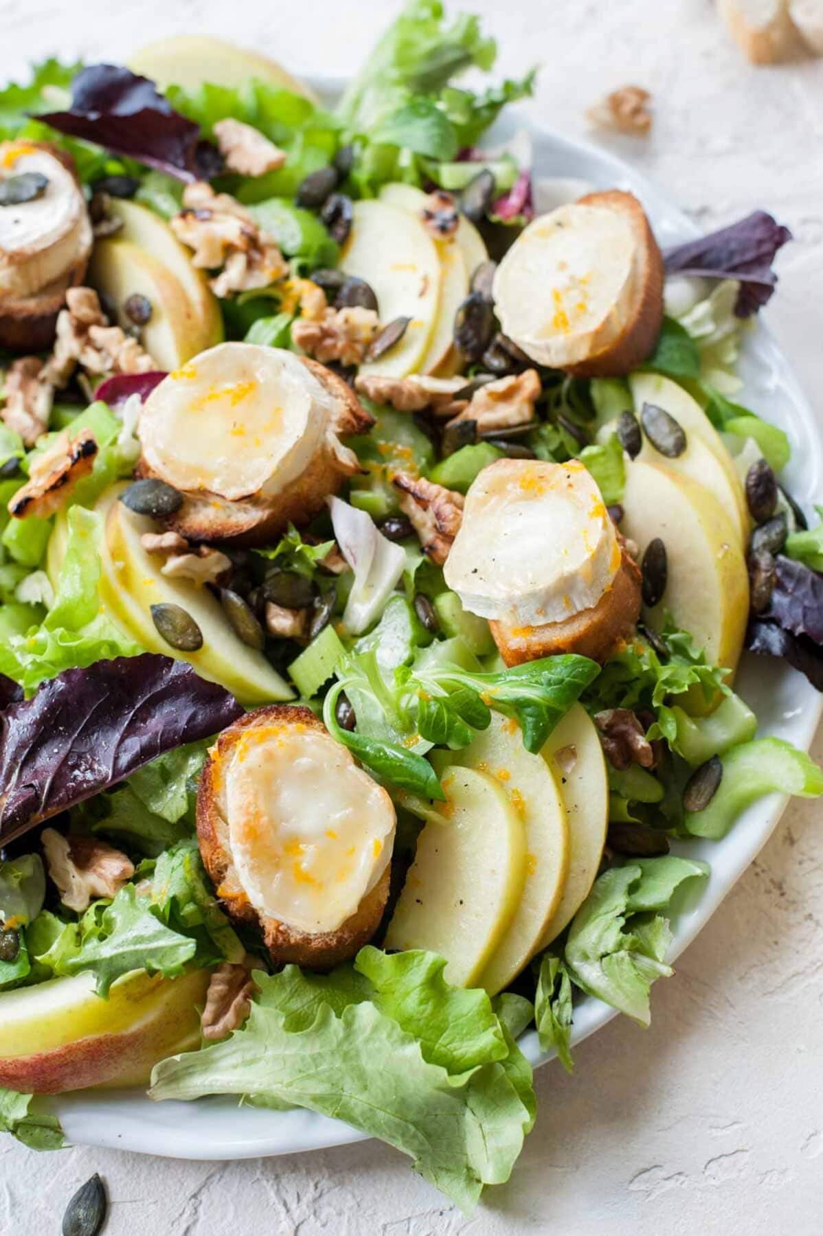 Close up picture of apple celery salad with walnuts and goat cheese on a white plate.