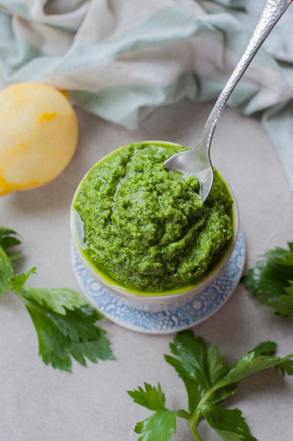 Celery leaf pesto being scooped out with a teaspoon from a small white ramekin.