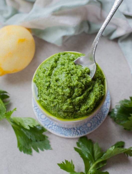 Celery leaf pesto being scooped with a teaspoon from a white ramekin.