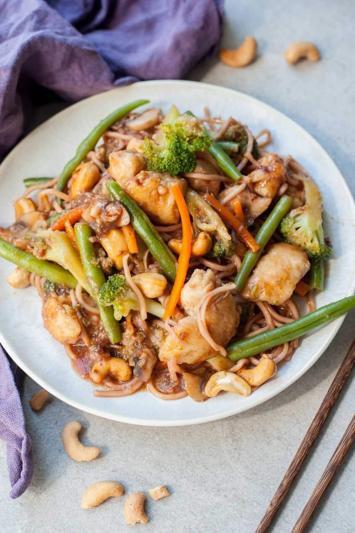 Chinese plum sauce noodles with chicken and veggies on a white plate, violet kitchen towel in the background