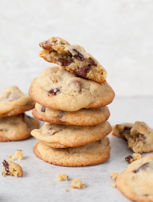 A stack of chocolate chip pecan cookies. Crumbled cookies scattered around.