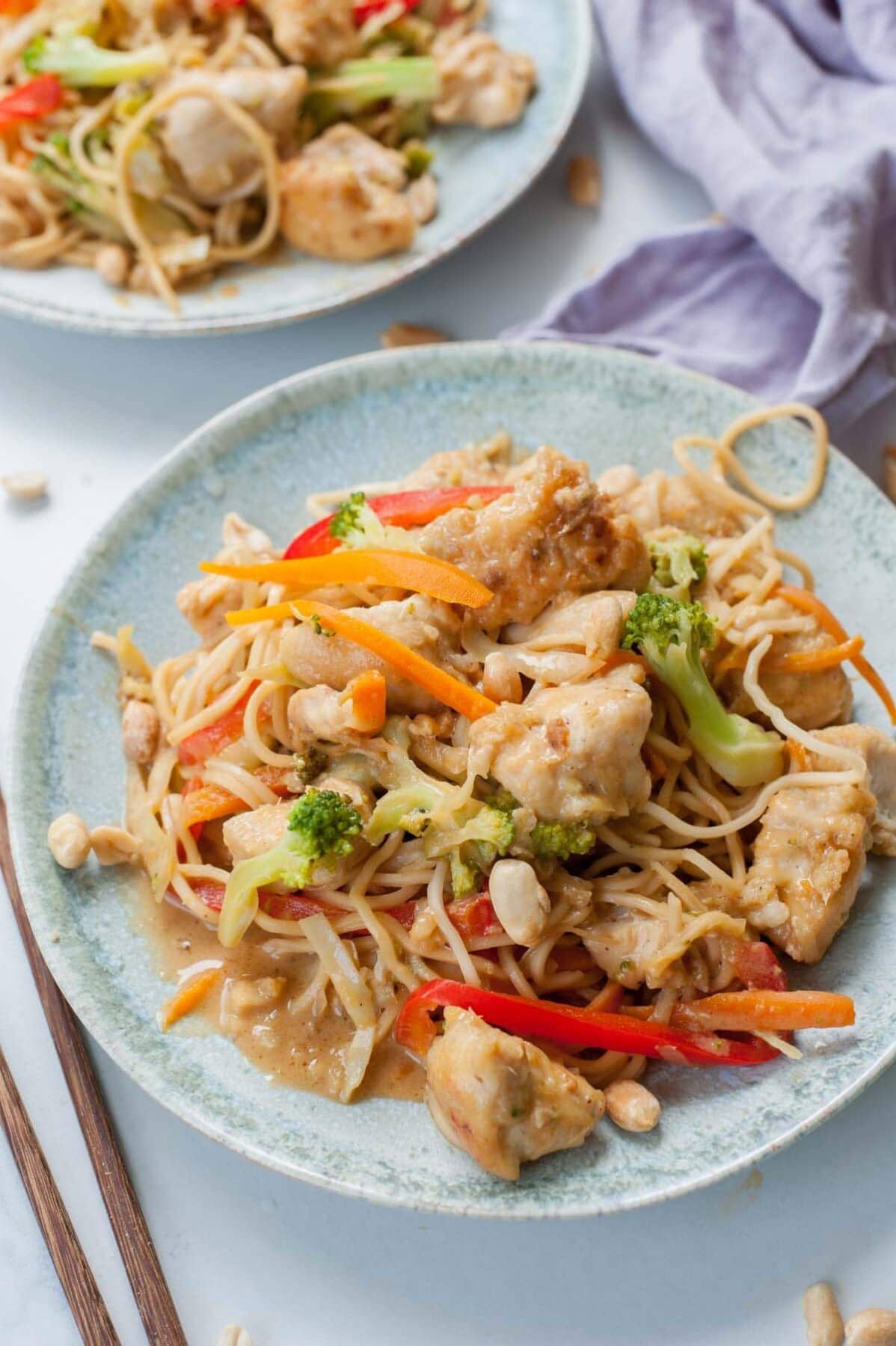 Peanut chicken noodles with vegetables and peanuts on a green plate