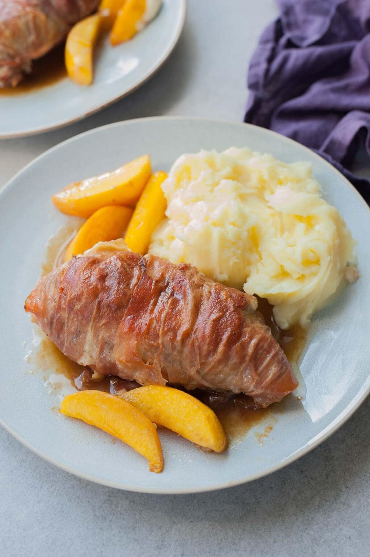 Prosciutto-wrapped chicken with peaches and balsamic glaze on a blue plate.