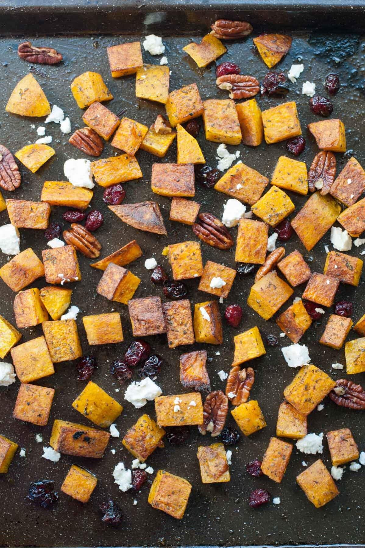 Roasted butternut squash with cranberries, rosemary, pecans, and feta on a black baking tray