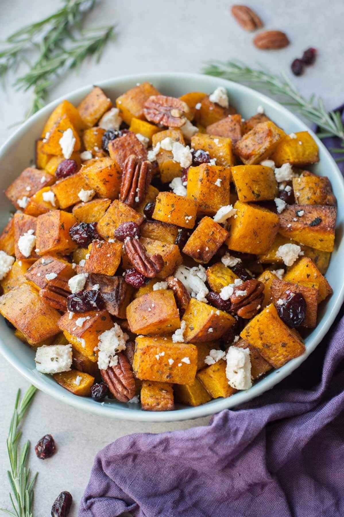 Roasted butternut squash with cranberries, rosemary, pecans, and feta in a blue bowl