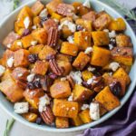 Roasted butternut squash with cranberries, pecans, rosemary and feta cheese in a blue bowl.