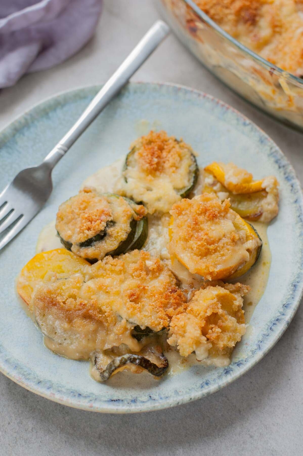 one serving of zucchini gratin on a blue plate with a fork on the side