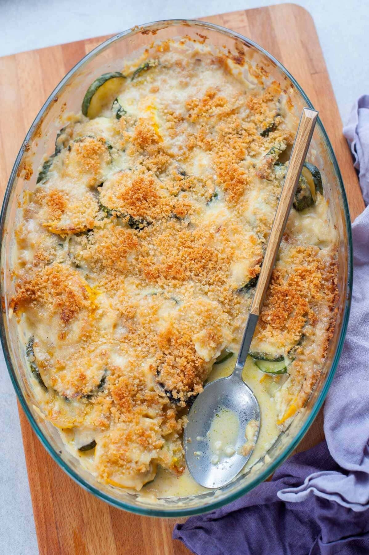 overhead picture of zucchini gratin in an oval glass baking dish on a chopping board