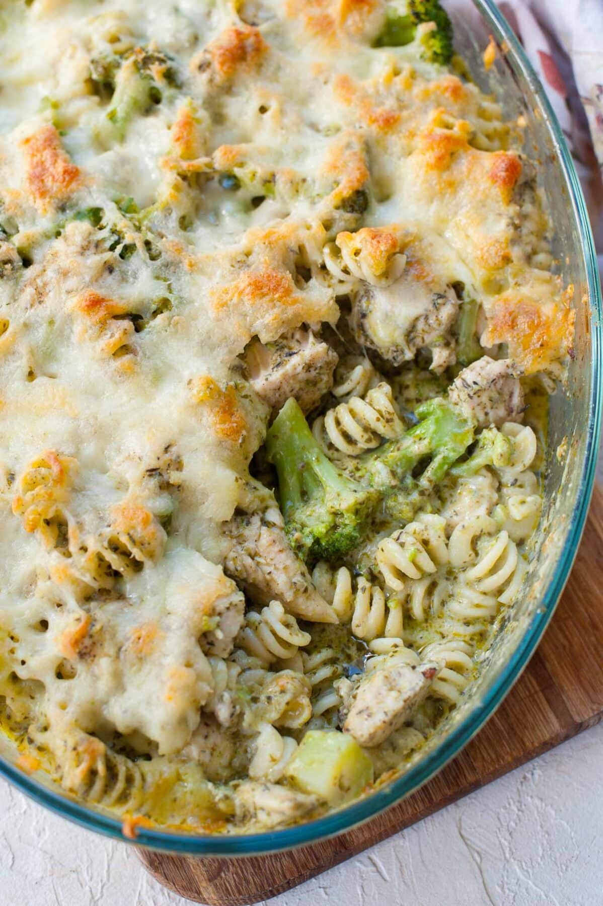 Pesto chicken bake in a casserole dish with a serving missing.