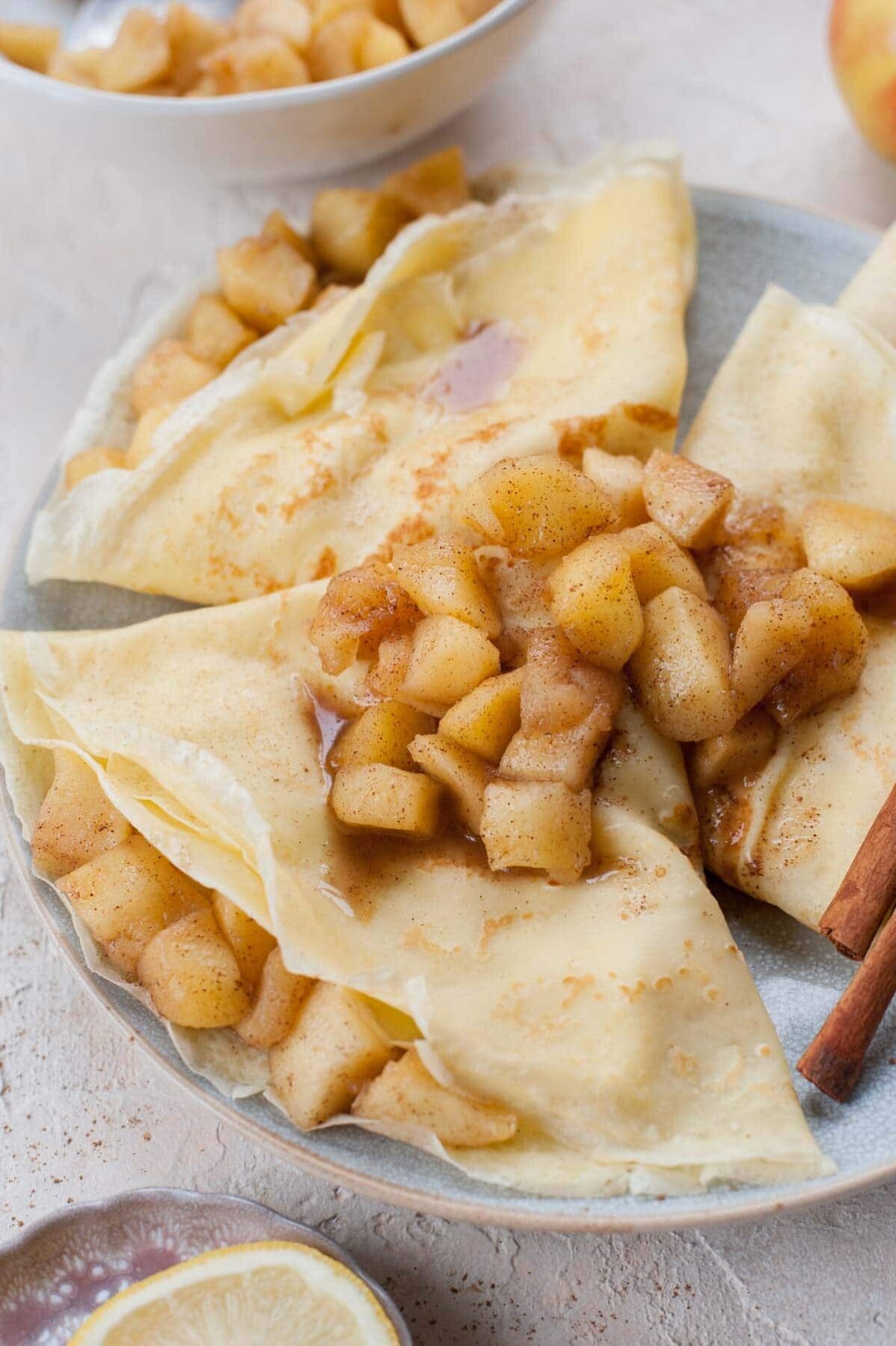 Close up photo of apple crepes on a blue plate topped with sauteed cinnamon apples.