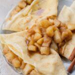 Apple crepes topped with sauteed apples on a blue plate.