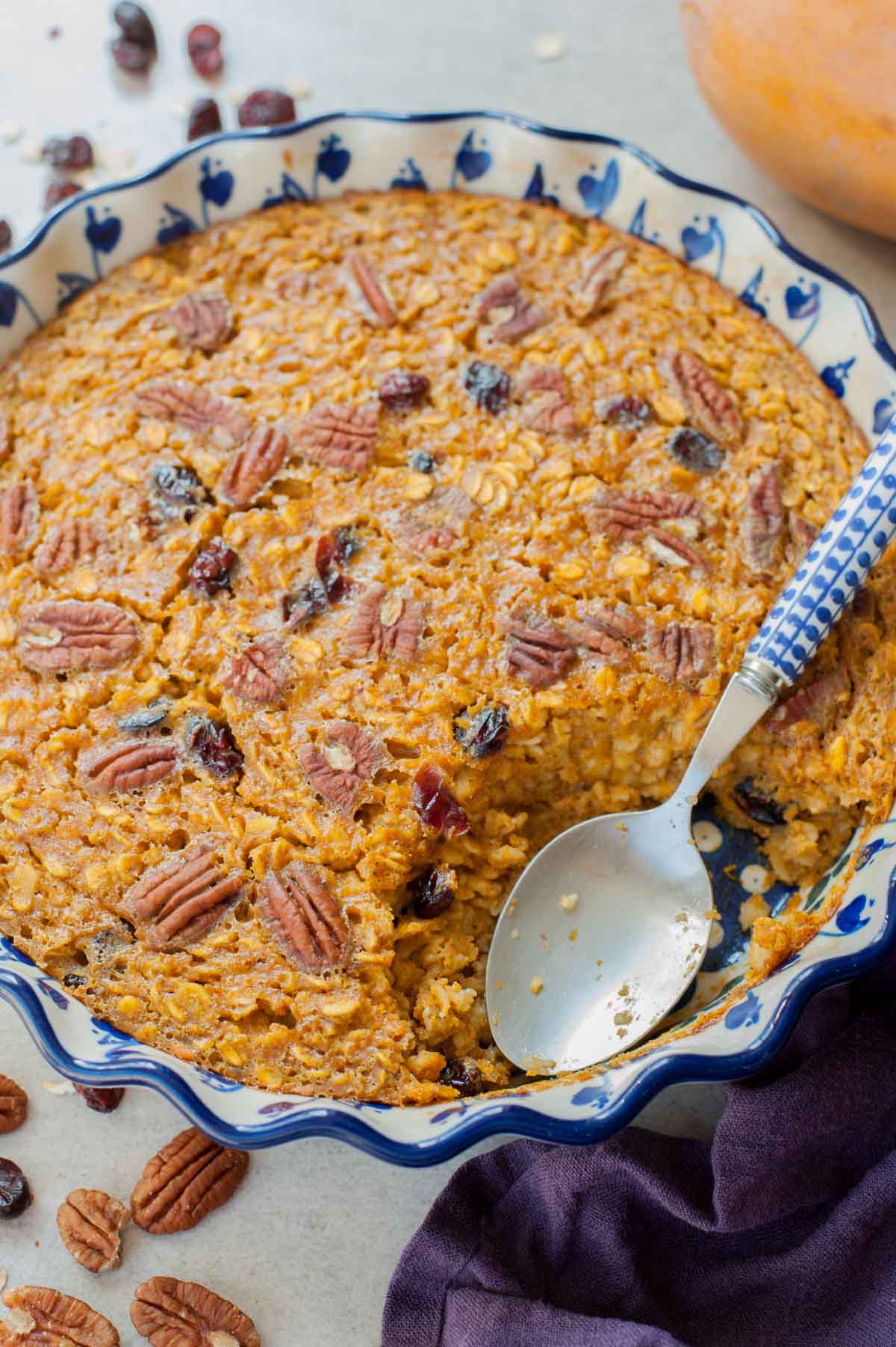 Close up picture of baked pumpkin oatmeal in a blue-white baking dish with a serving missing.