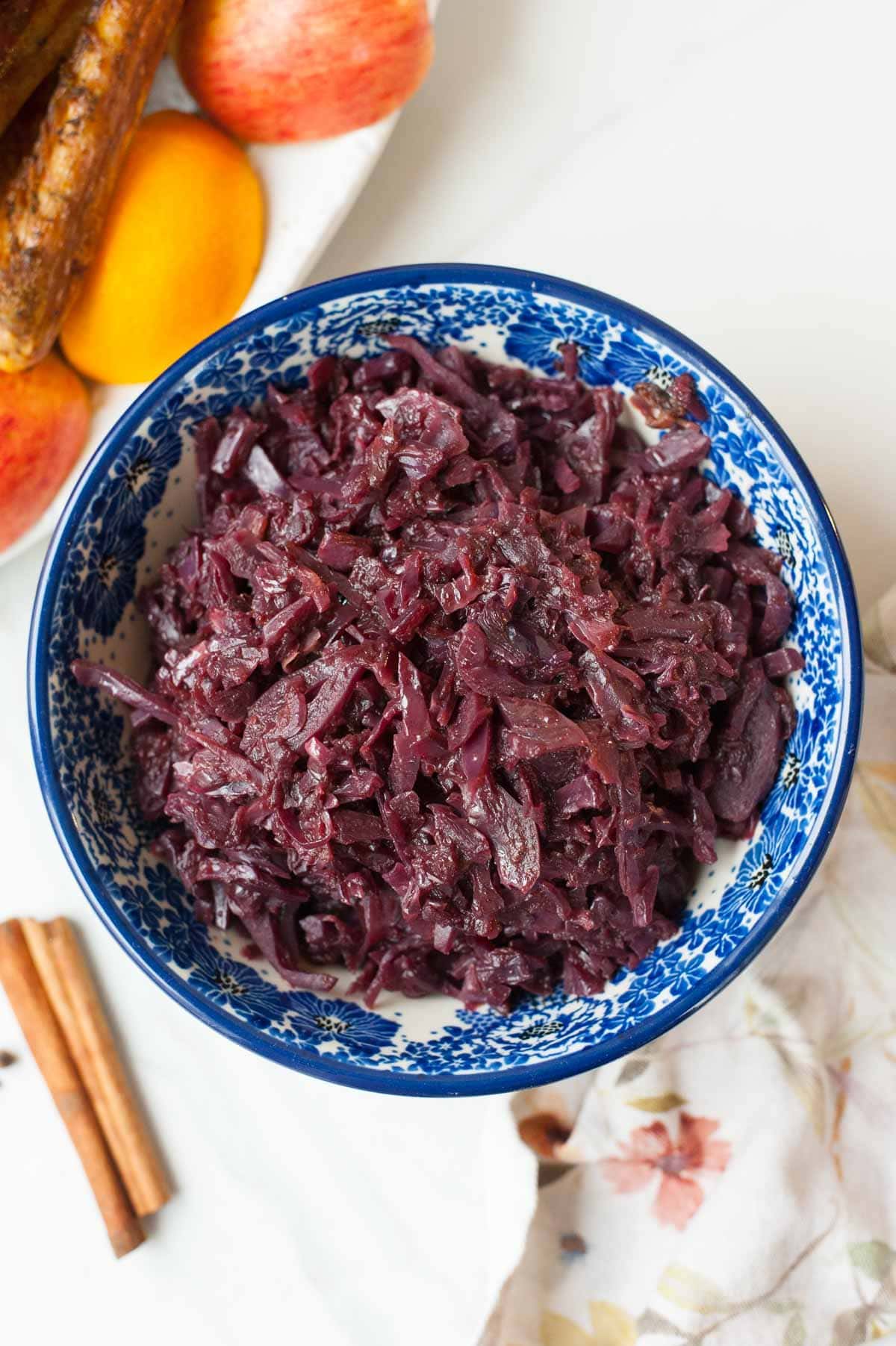 Braised red cabbage with apples in a blue bowl. Roast goose in the background.