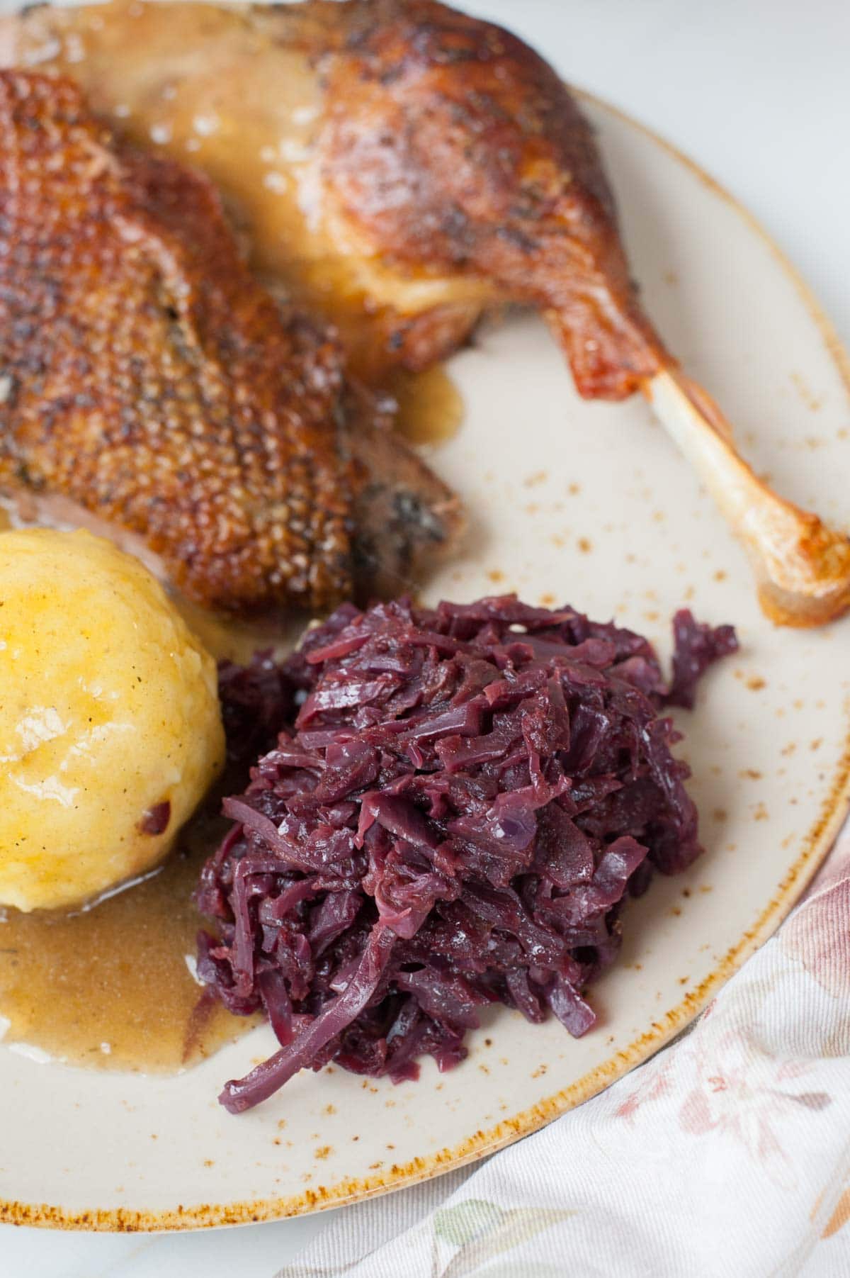 Braised red cabbage with apples on a brown plate served with roast goose, and potato dumplings.