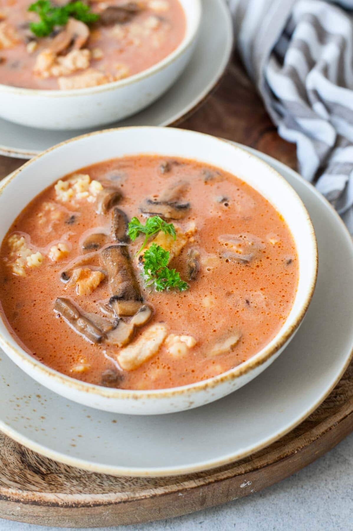 Chicken tomato soup with mushroom served with pasta and parsley in a white bowl.