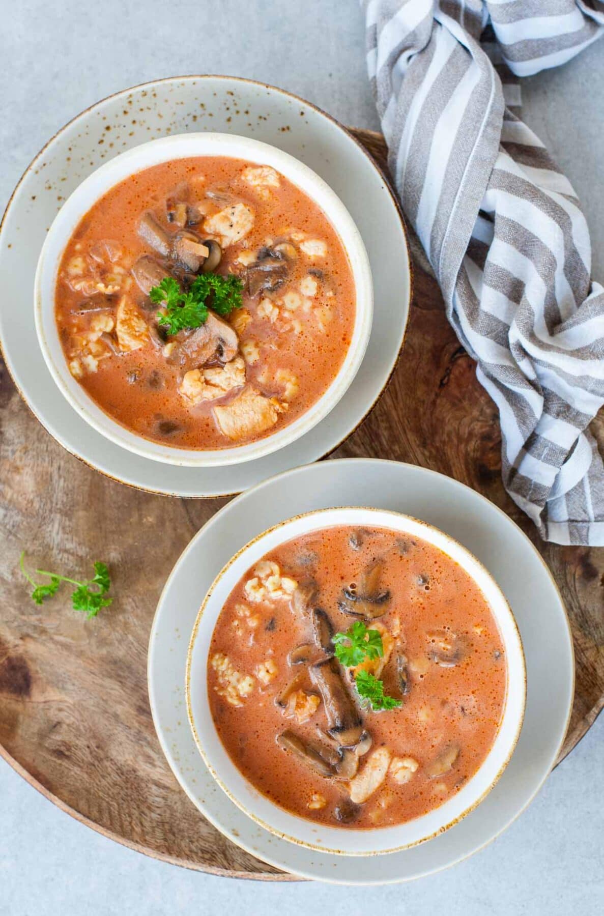 Two bowls with chicken tomato soup with mushrooms served with pasta and parsley.