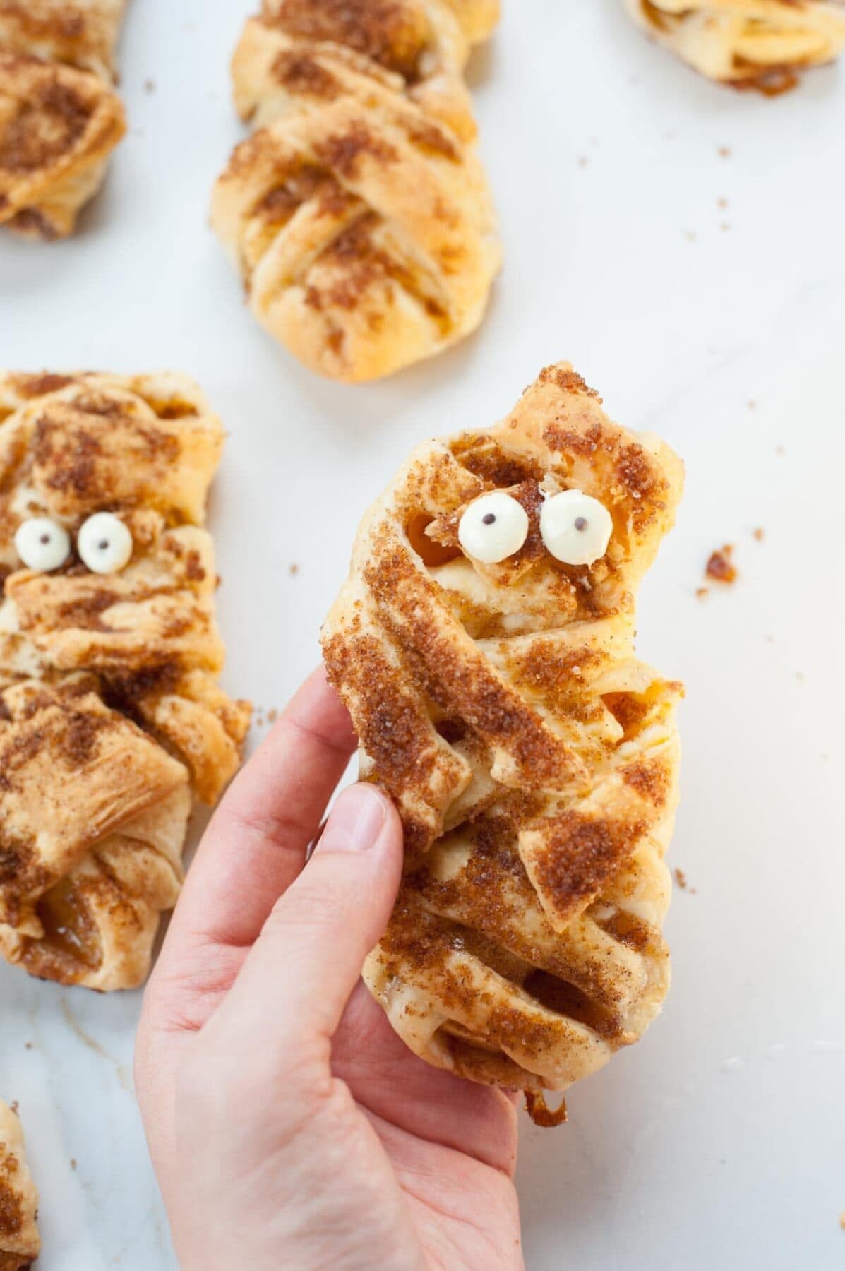 Mummy puff pastry apple pastries held in a hand.