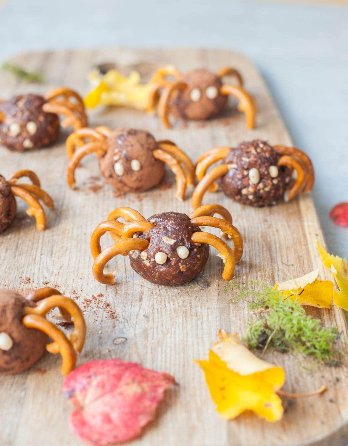 Pretzel spiders on a chopping board. Leaves scattered around.