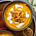 Pumpkin chestnut soup in a black bowl topped with yogurt and caramelized chestnuts.