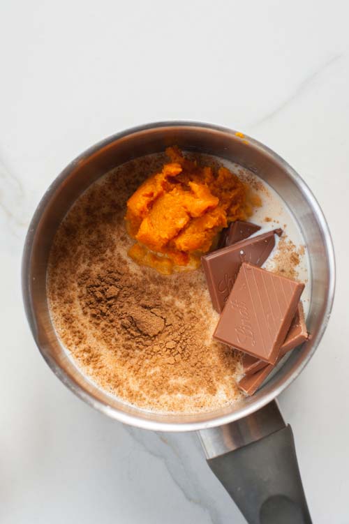 Ingredients for pumpkin spice hot chocolate in a small pot.