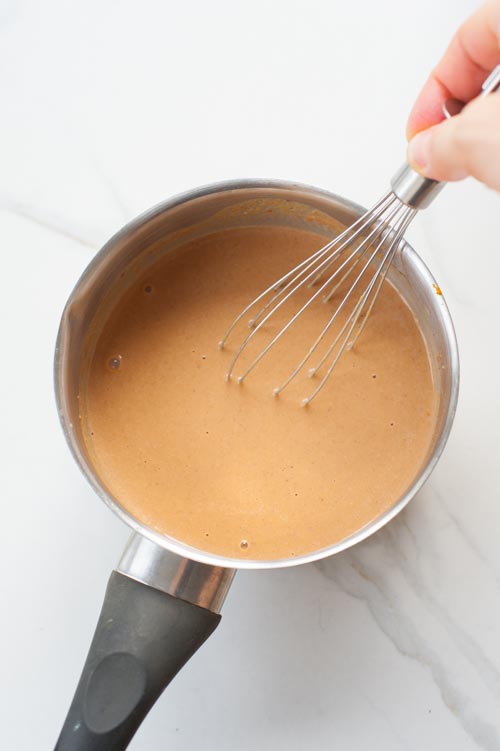 Pumpkin spice hot chocolate in a pot is being whisked.