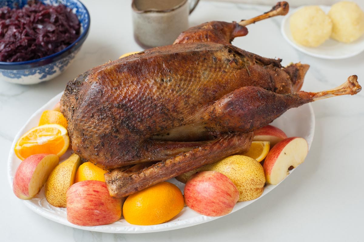 Roast goose on a white plate with apple, orange, and pear quarters scattered around.