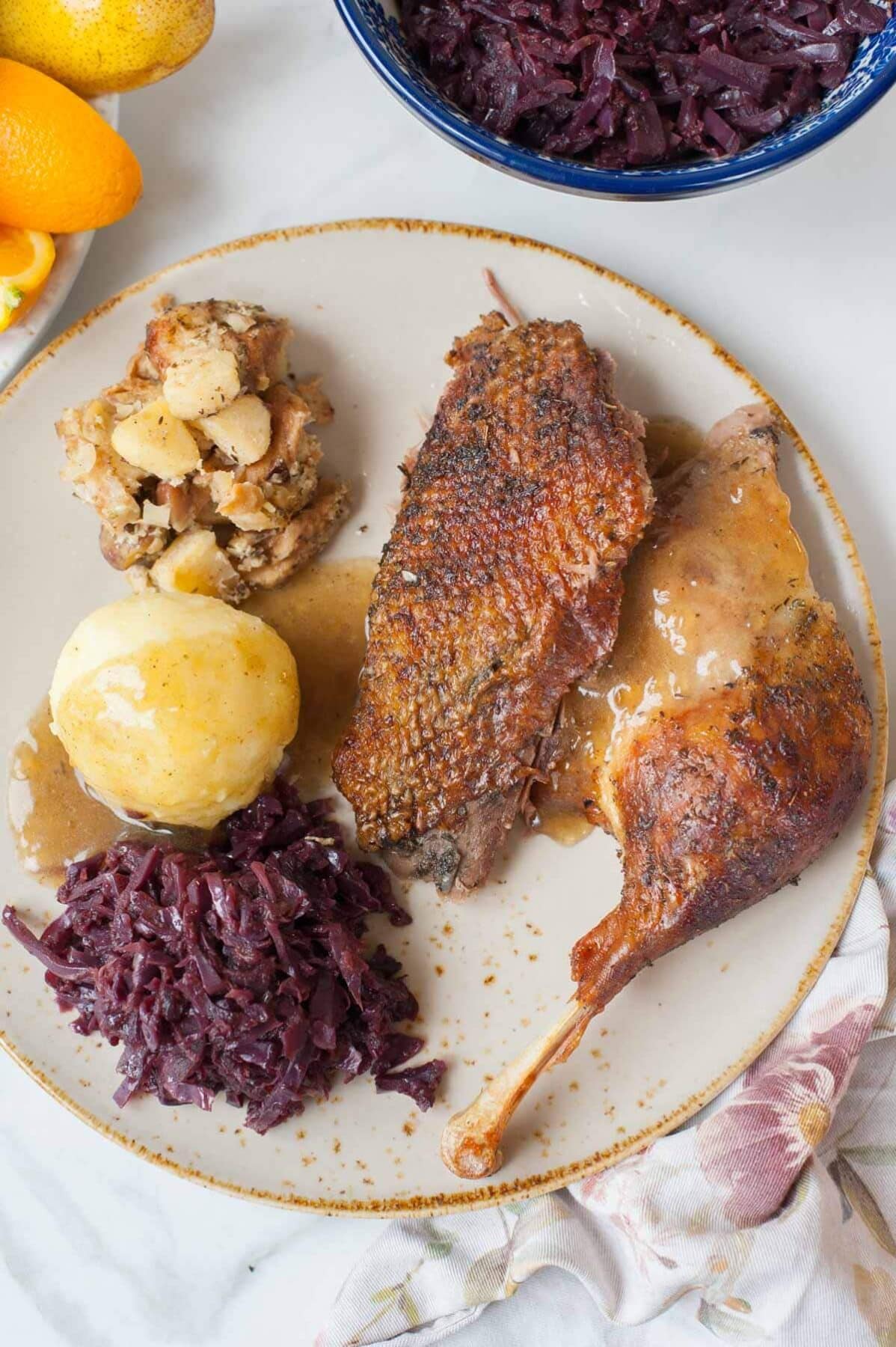 Goose breast and leg on a brown plate with stuffing, potato dumpling, braised red cabbage, and gravy.