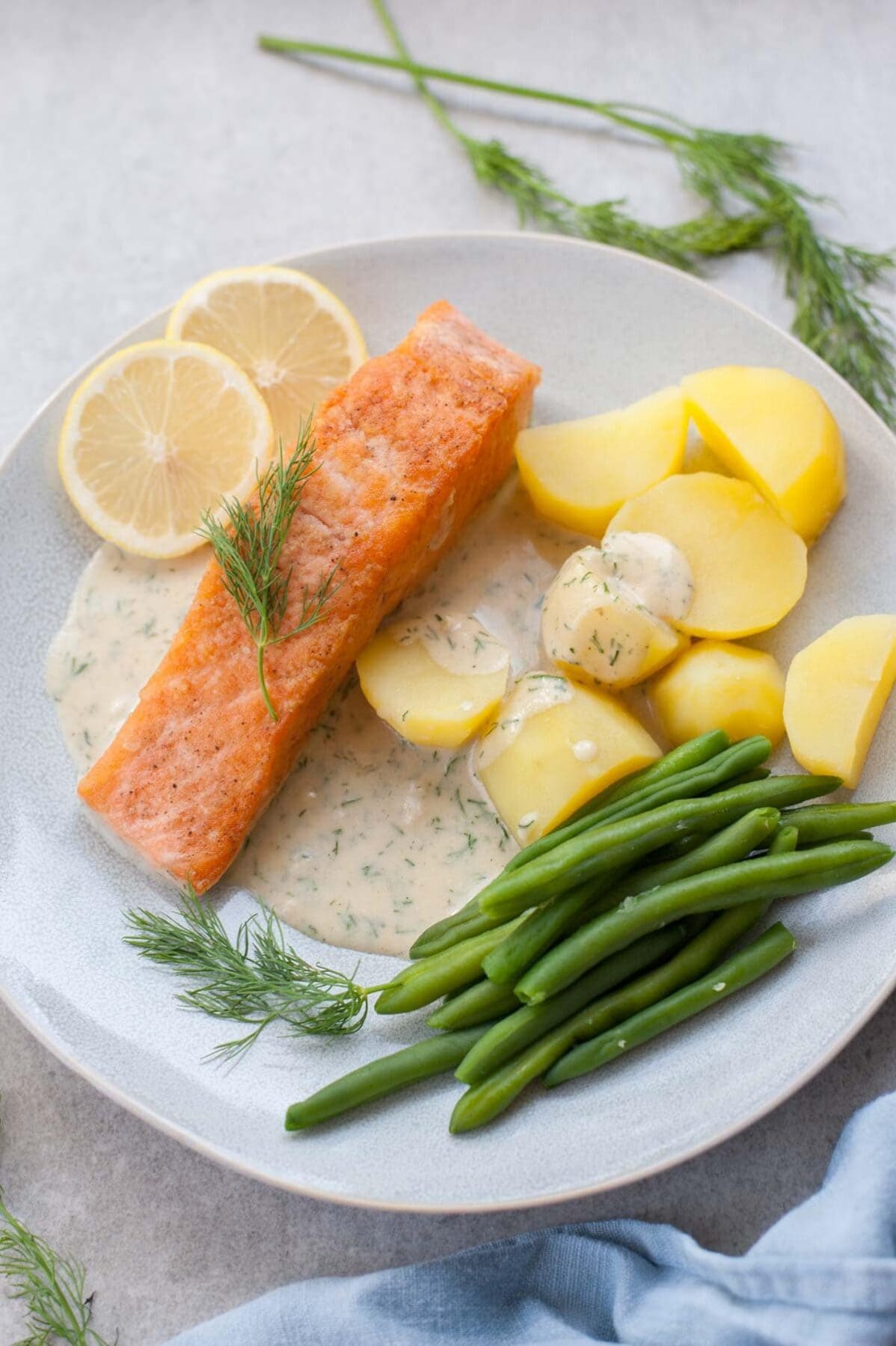 Salmon with creamy dill sauce, potatoes and green beans on a white plate.