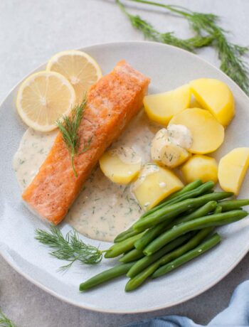 Salmon with creamy dill sauce, potatoes, and green beans on a blue plate.