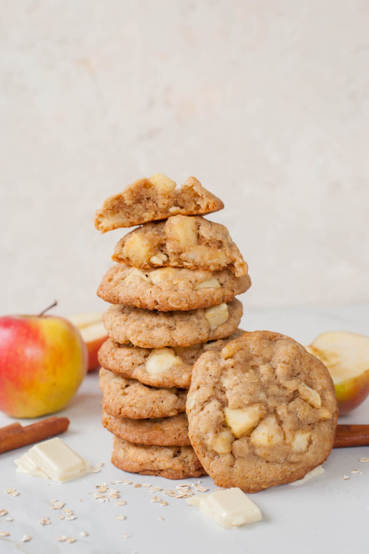 A stack of apple cinnamon oatmeal cookies. White chocolate, oats and apples scattered around.