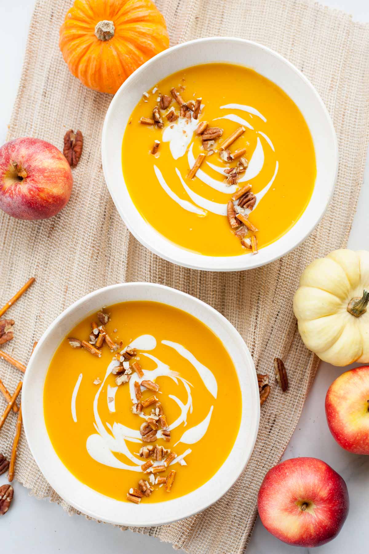 Two white bowls with butternut squash apple soup topped with yogurt and pretzels.