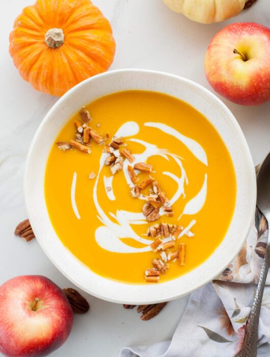 White bowl with butternut squash and apple soup. Apples in the background.