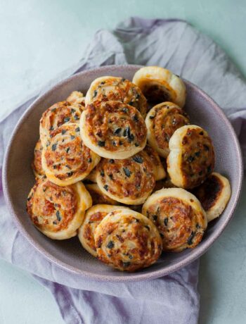 Cheese olive and sun-dried tomato puff pastry pinwheels in w violet bowl.