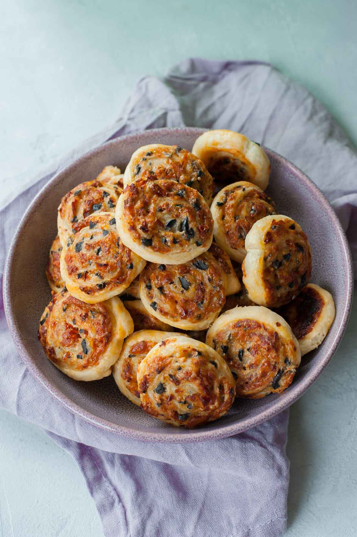 Cheese olive and sun-dried tomato puff pastry pinwheels in w violet bowl.