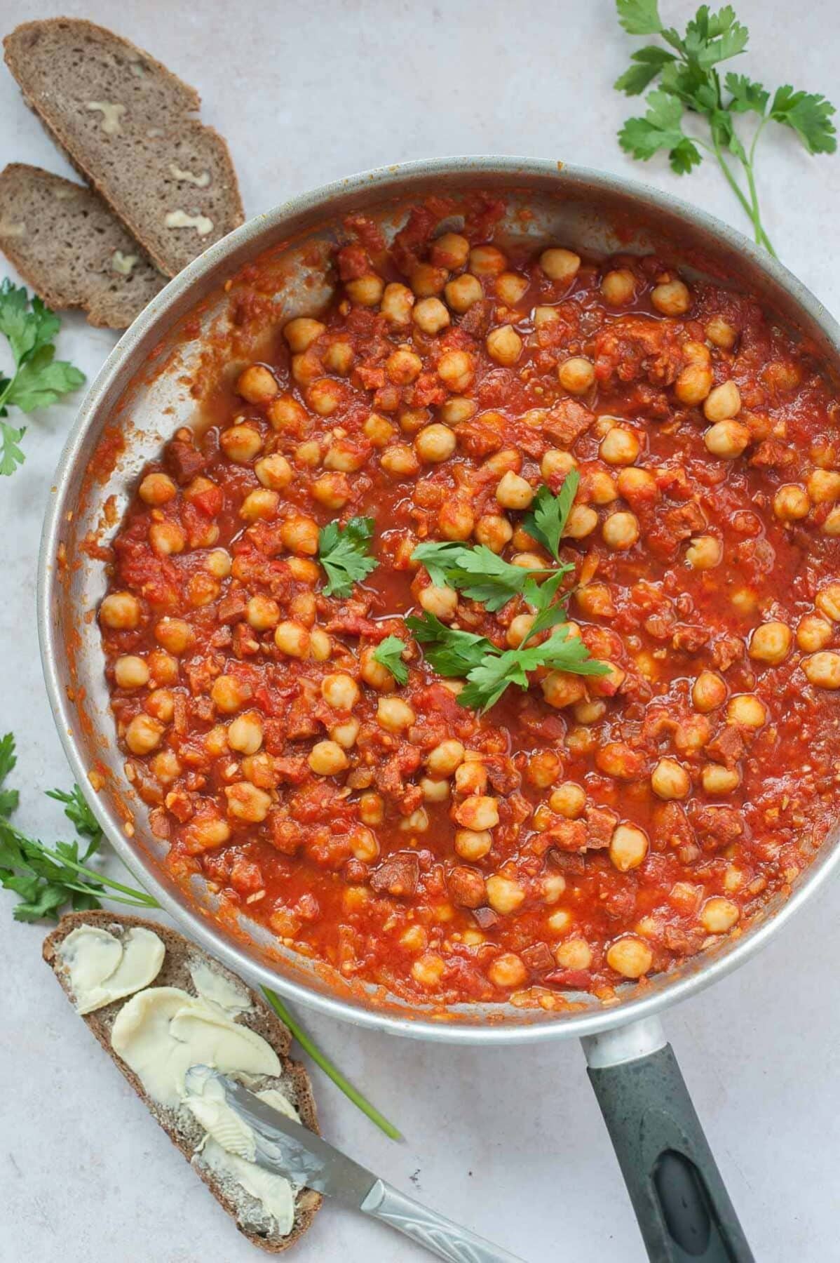 Chickpeas with chorizo in tomato sauce in a silver frying pan.