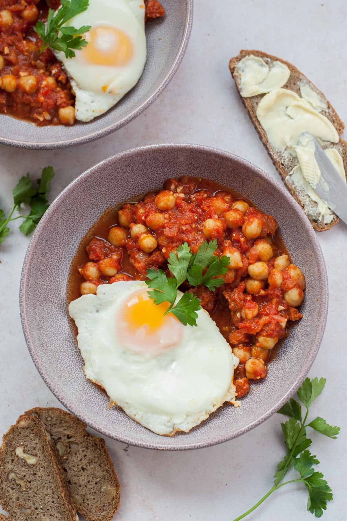 Chickpeas with chorizo in tomato sauce in a violet bowl with a side of sunny-side-up egg.