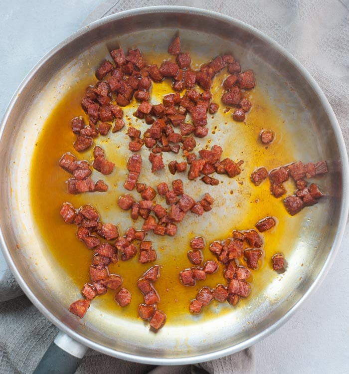 Cooked chorizo and fat released from chorizo in a frying pan.