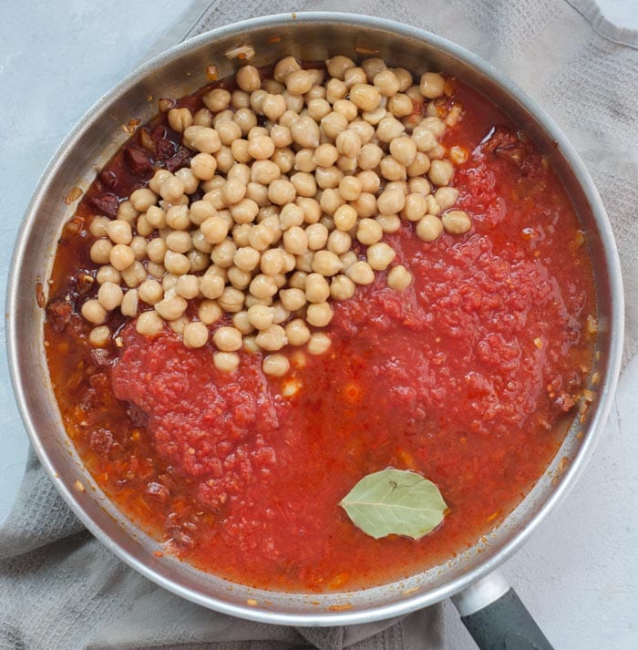 Chickpeas, chorizo cooked with onions and crushed tomatoes in a frying pan.