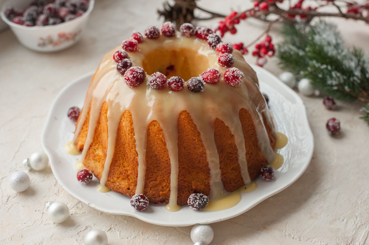 Cranberry orange bundt cake with white chocolate glaze, topped with sugared cranberries, on a white plate.