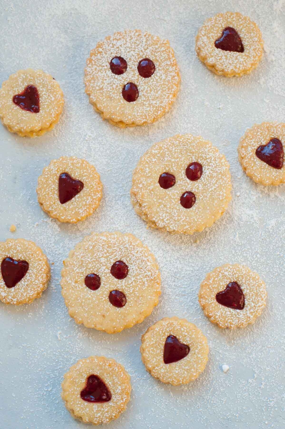 Ciastka Linzer w kształcie serca i z trzema kółkami w środku na niebieskim tle.