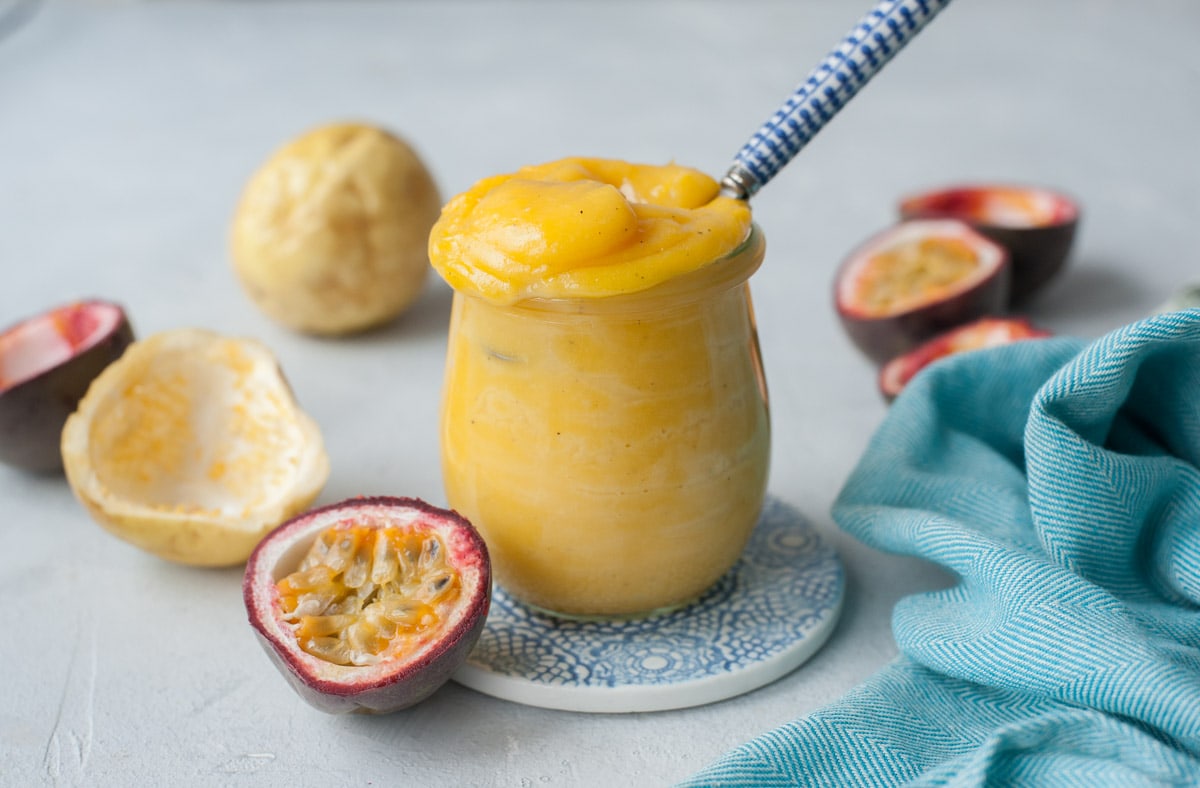 Passion fruit curd in a jar. Passion fruits and a blue kitchen cloth in the background.