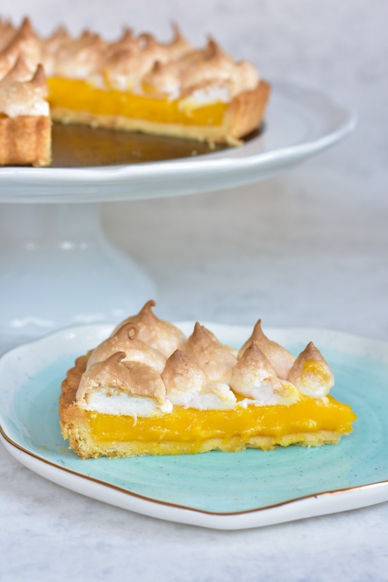 A piece of passion fruit tart on a blue plate. Whole tart in the background.