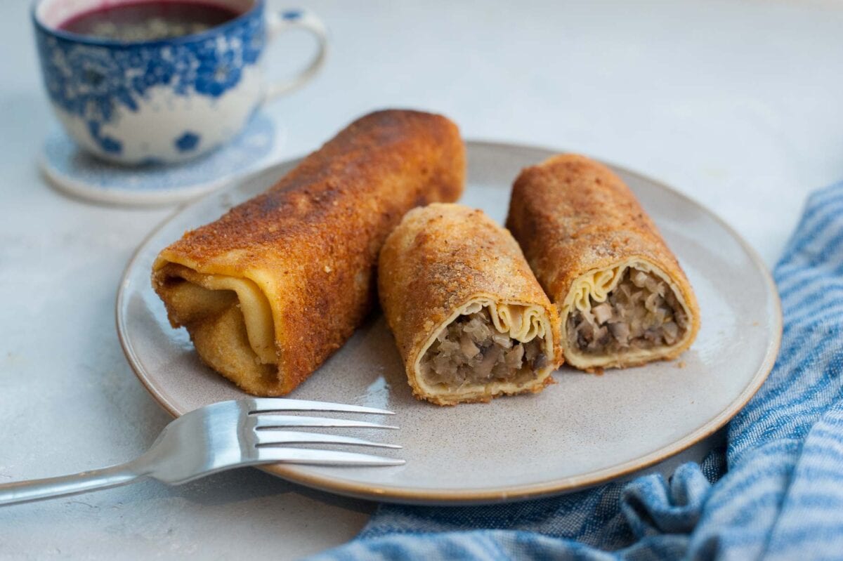 Polish krokiety on a brown plate with a fork on the side. Blue cup in the background.