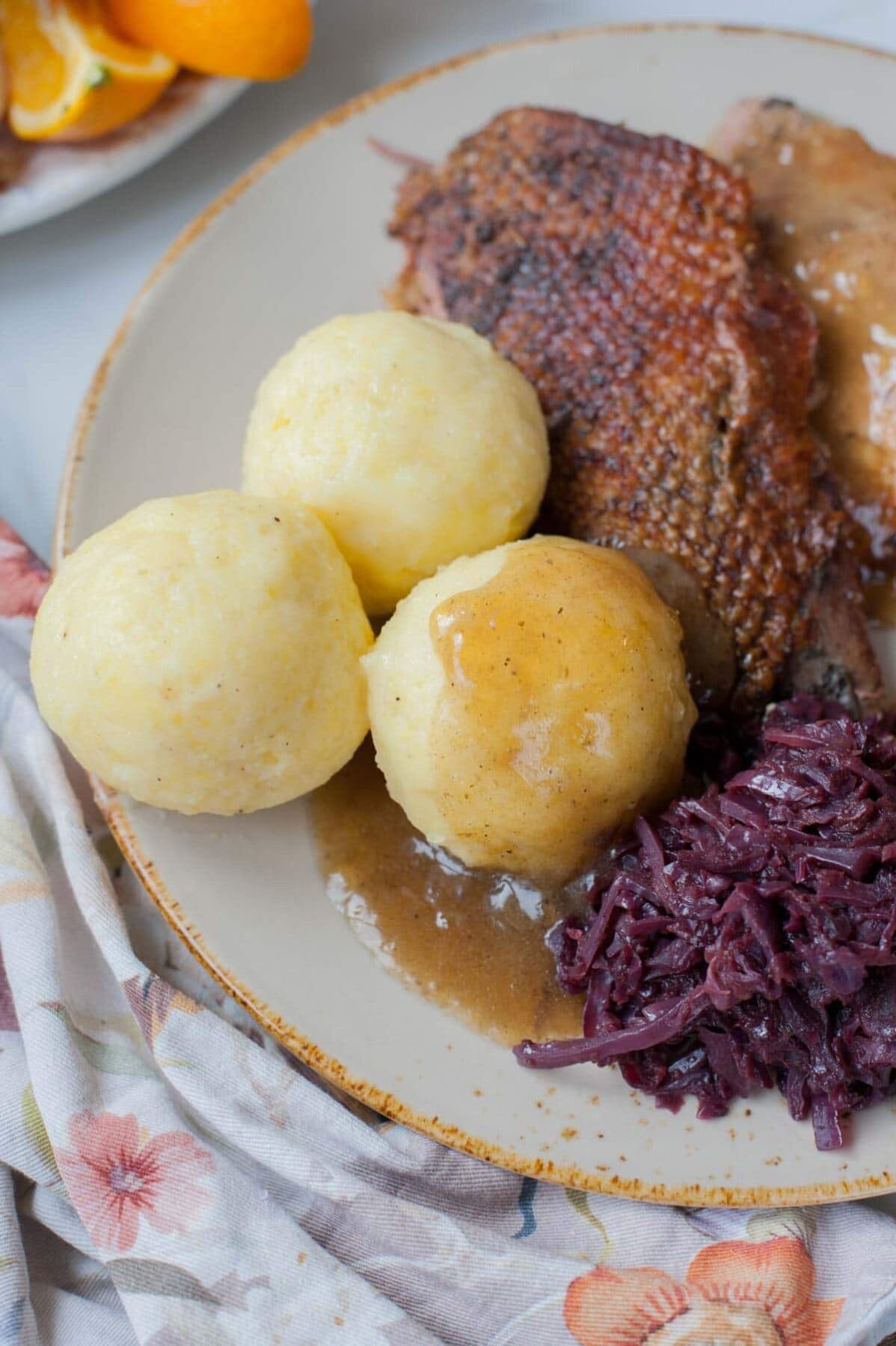 Potato dumplings on a brown plate with braised cabbage and roast goose breast.