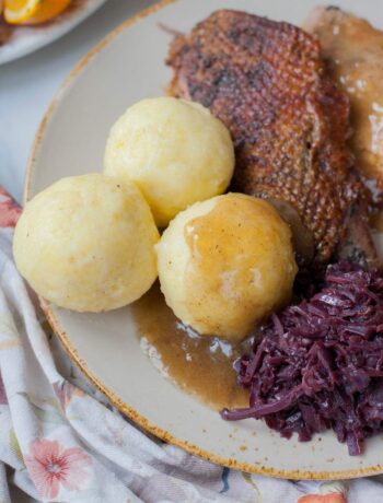 Potato dumplings on a brown plate with braised cabbage and roast goose.