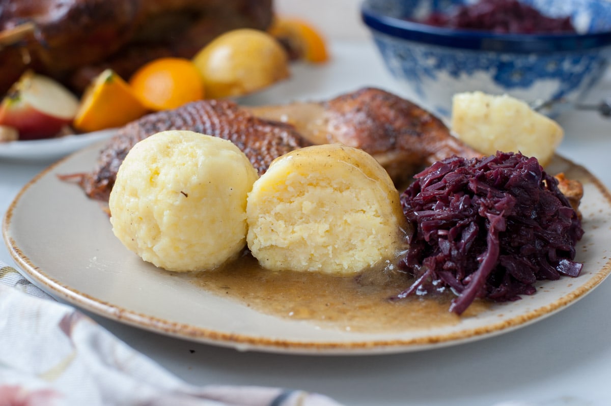 Potato dumplings cut in half on a brown plate with braised cabbage and roast goose.