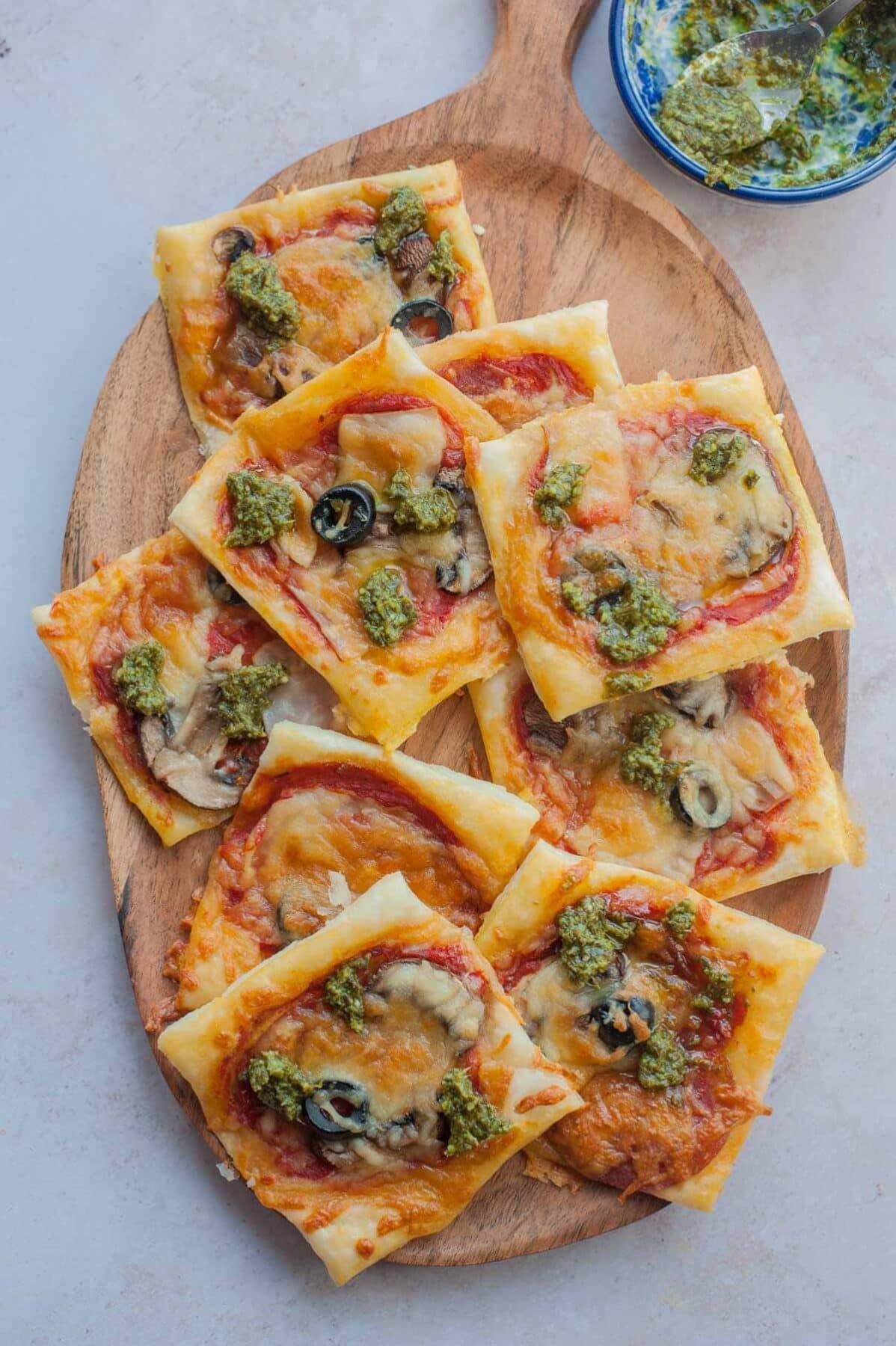 Puff pastry pizza bites on a wooden serving tray.