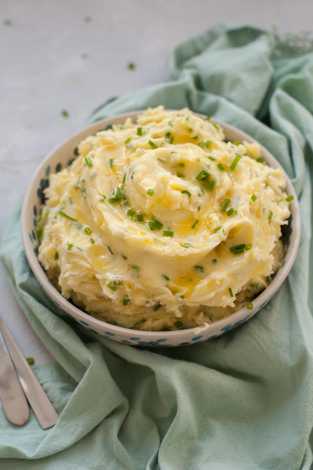 Sour cream mashed potatoes topped with melted butter and chives in a white-blue bowl.