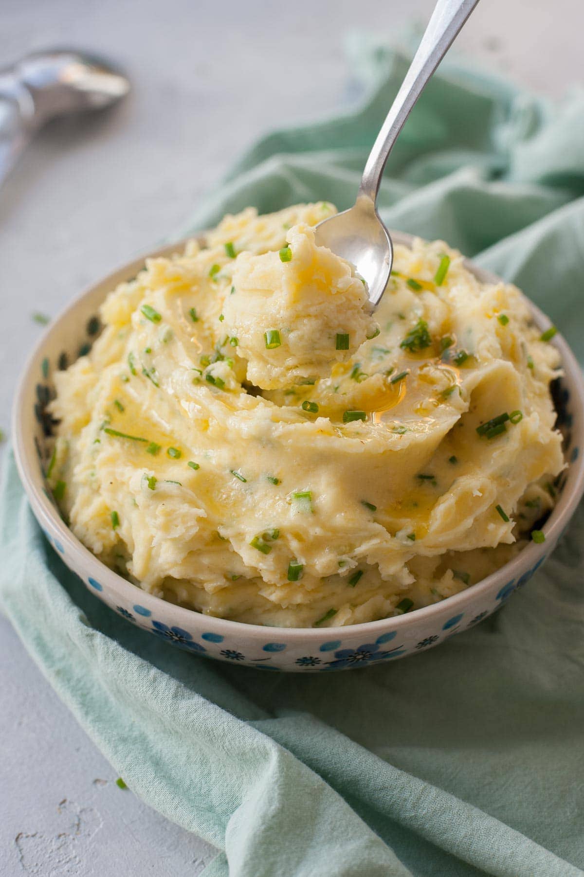 Sour cream mashed potatoes with chives in a blue bowl. Green kitchen cloth underneath.