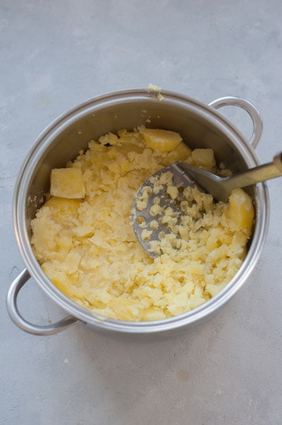 Cooked potatoes are being mashed in a pot.